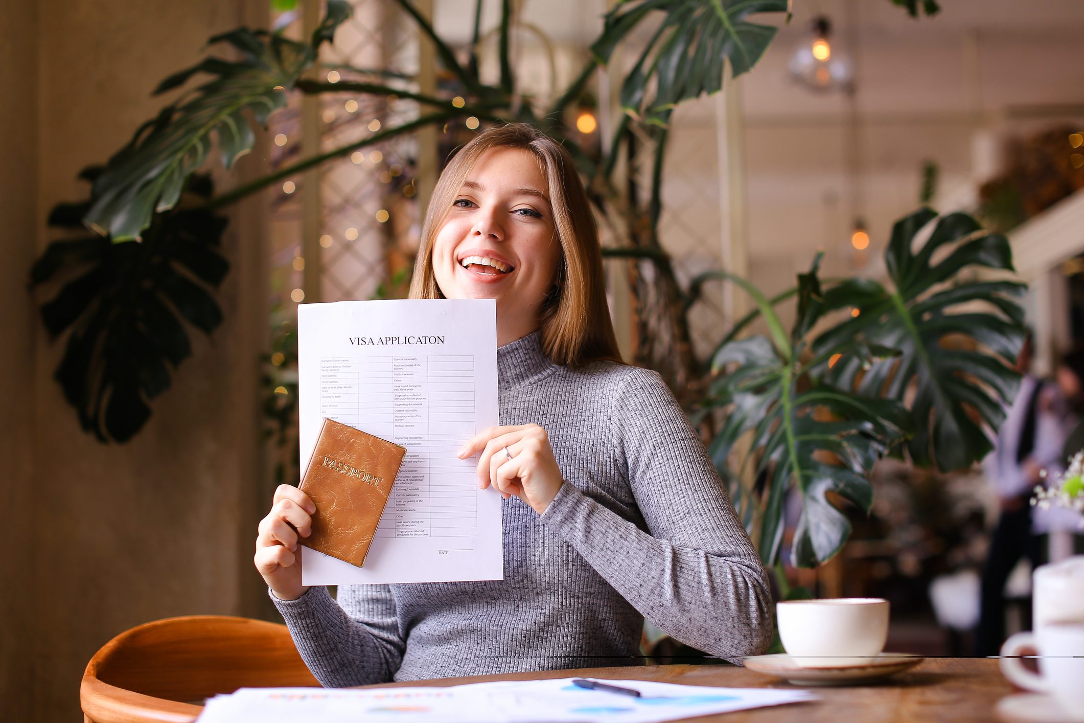 Pretty girl holding passport and visa application at travel agency cabinet Pretty young woman holding passport and visa application at travel agency cabinet, monstera in background. Concept of execution of documents and traveling.